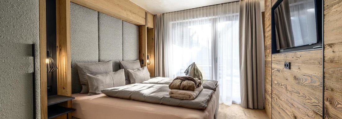 A modern bedroom with a large bed and wooden paneling. The room has large windows and a television on the wall. - The Peak Sölden - Sölden