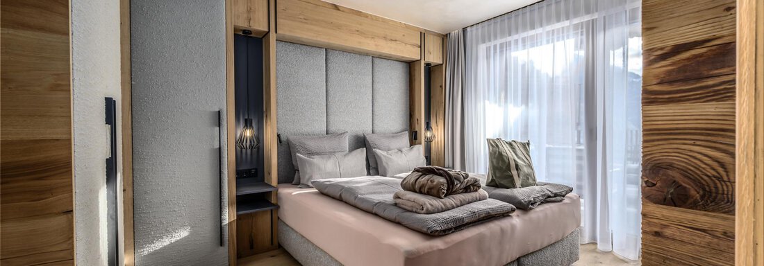 A modern bedroom with a large bed and cozy pillows. The walls are made of wood, and large windows let in plenty of light. - The Peak Sölden - Sölden