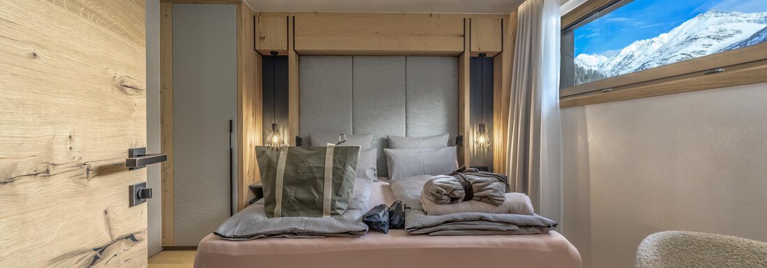 A modern bedroom with a cozy bed and large windows. Through the window, there is a beautiful view of the mountains. - The Peak Sölden - Sölden