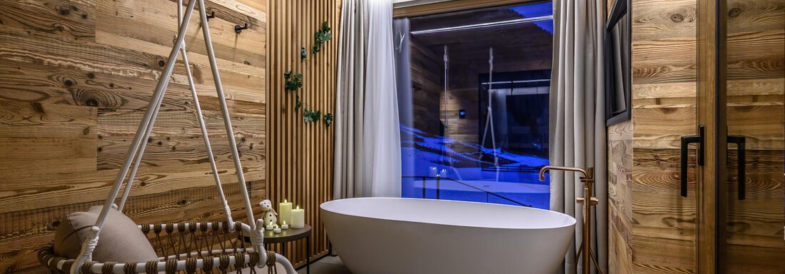 A modern bathroom with a freestanding bathtub and a hanging chair. Warm wood and large windows create a cozy atmosphere. - The Peak Sölden - Sölden