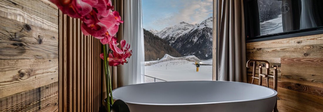 A modern bathroom with a freestanding bathtub and wood paneling. Through the window, a stunning mountain landscape can be seen. - The Peak Sölden - Sölden