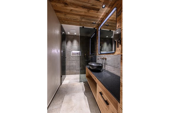 A modern bathroom with a wooden ceiling and elegant stone sink. The shower is separated by glass walls and the decor is simple and stylish. - The Peak Sölden - Sölden