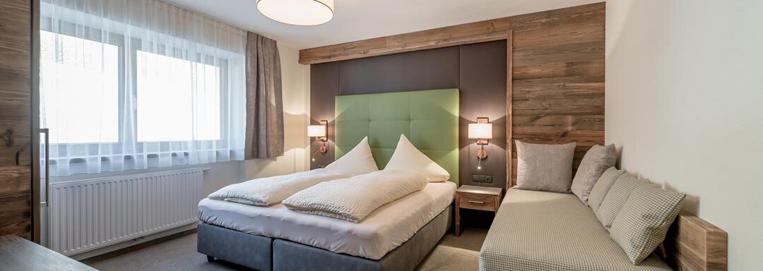 A modern room with a double bed and a cozy seating area.  
Large windows provide plenty of daylight and an inviting atmosphere. - The Peak Sölden - Sölden