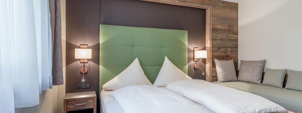 A modern bedroom with a double bed and a cozy sitting area. The walls are painted in natural tones, and the lighting creates a pleasant atmosphere. - The Peak Sölden - Sölden