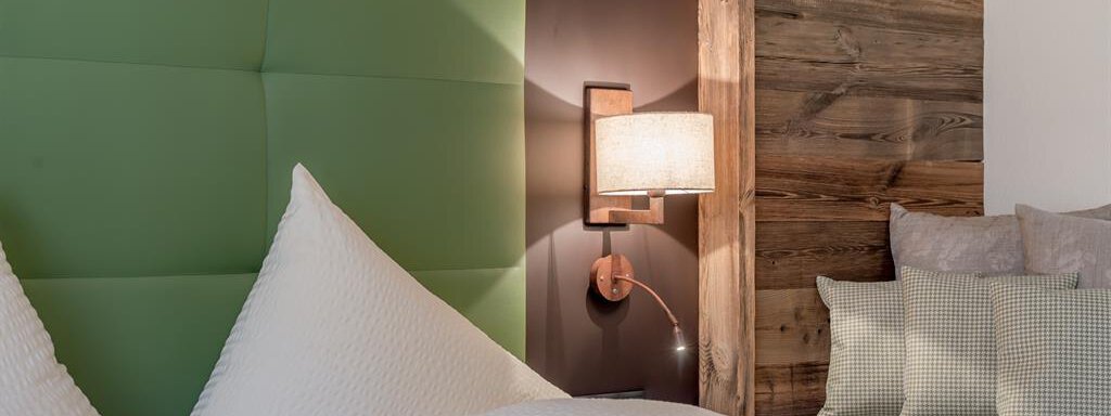 A modern bedroom with a green headboard and warm wood. The bedding is white and the lighting creates a cozy atmosphere. - The Peak Sölden - Sölden