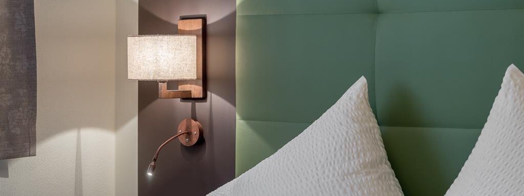 A cozy bedroom with a large, green headboard. Next to the bed is a modern wall lamp. - The Peak Sölden - Sölden
