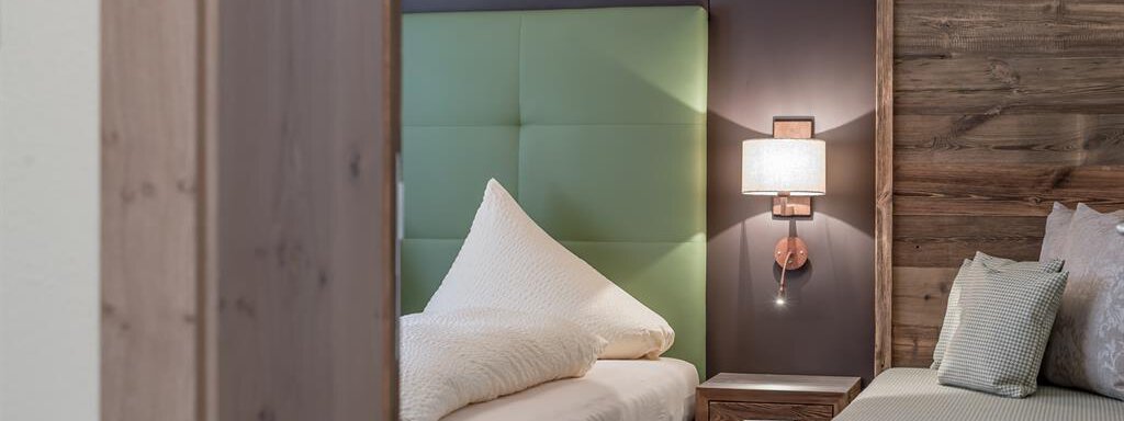 A modern bedroom with two beds. The walls are made of wood, and a green wall paneling provides a fresh accent. - The Peak Sölden - Sölden