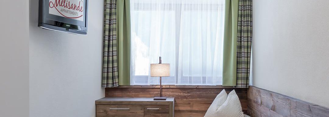 A cozy room with a single bed, a nightstand, and a television. Large windows with light curtains allow for plenty of daylight. - The Peak Sölden - Sölden