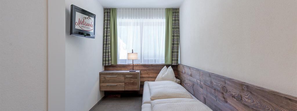 A simple room with a bed, a television, and a nightstand.  
Large windows with curtains bring a lot of light into the room. - The Peak Sölden - Sölden