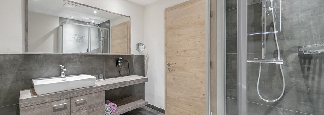 A modern bathroom with an elegant shower and a simple sink. Bright walls and wooden accents create an inviting atmosphere. - The Peak Sölden - Sölden