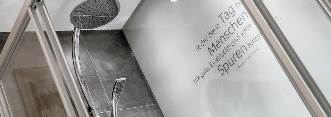 A modern shower with a stylish overhead shower. Inspirational texts can be seen on the wall. - The Peak Sölden - Sölden