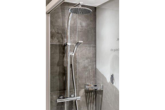 A modern shower faucet with a large rainfall showerhead and handheld shower. The walls are designed with elegant gray tiles. - The Peak Sölden - Sölden