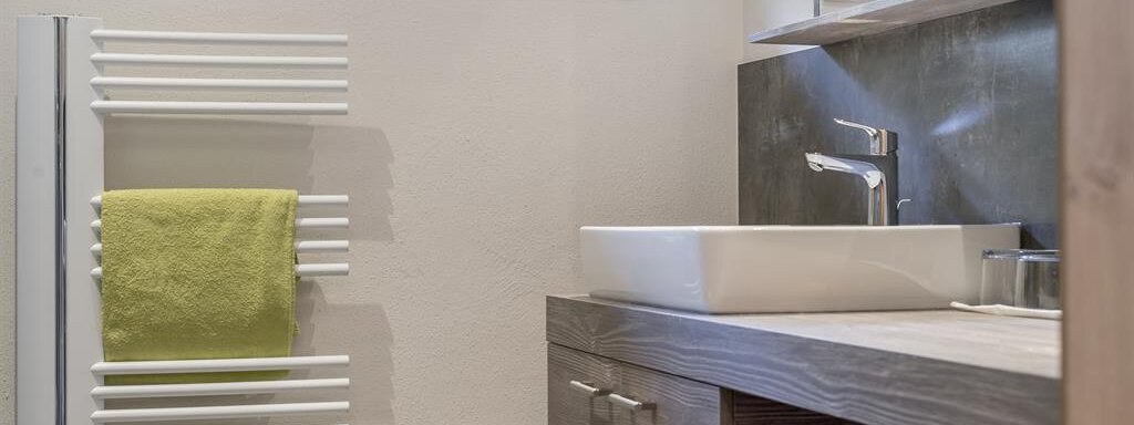 A modern bathroom with a sink and a wooden cabinet. Towels in fresh colors hang on a towel warmer. - The Peak Sölden - Sölden