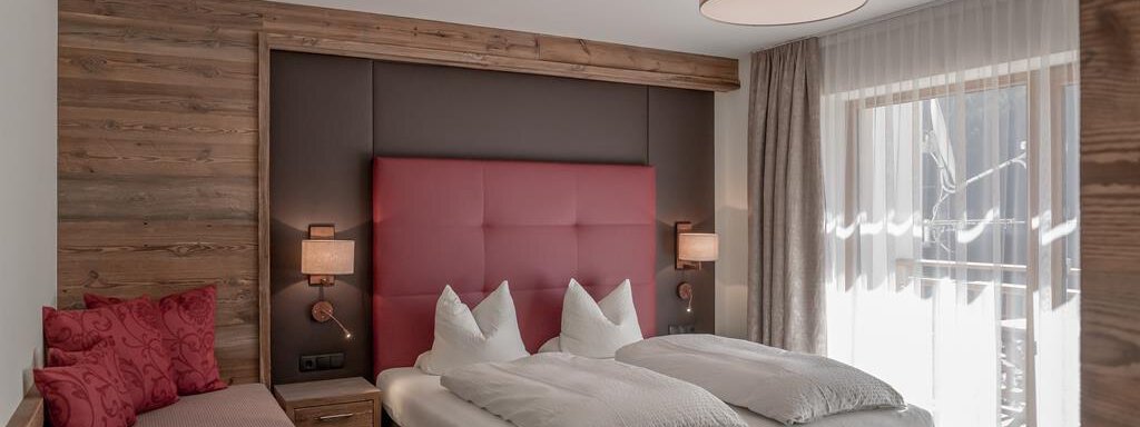 Schlafzimmer A cozy hotel room with a large double bed and a small sofa. The walls are paneled with wood, and there are large windows with a view outside. - The Peak Sölden - Sölden