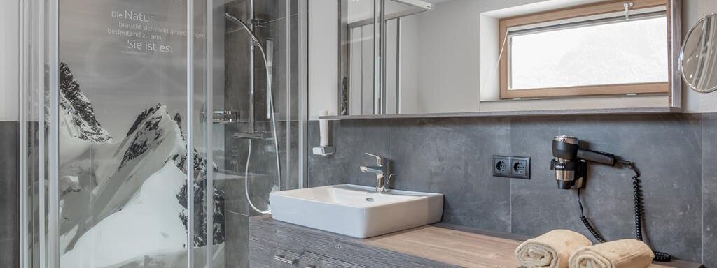A modern bathroom with a glass shower and an elegant sink. The walls are in neutral colors, and the windows let in plenty of daylight. - The Peak Sölden - Sölden