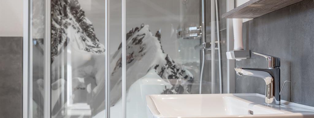 A modern bathroom with an elegant sink and a glass shower. In the background, snow-covered mountains can be seen. - The Peak Sölden - Sölden