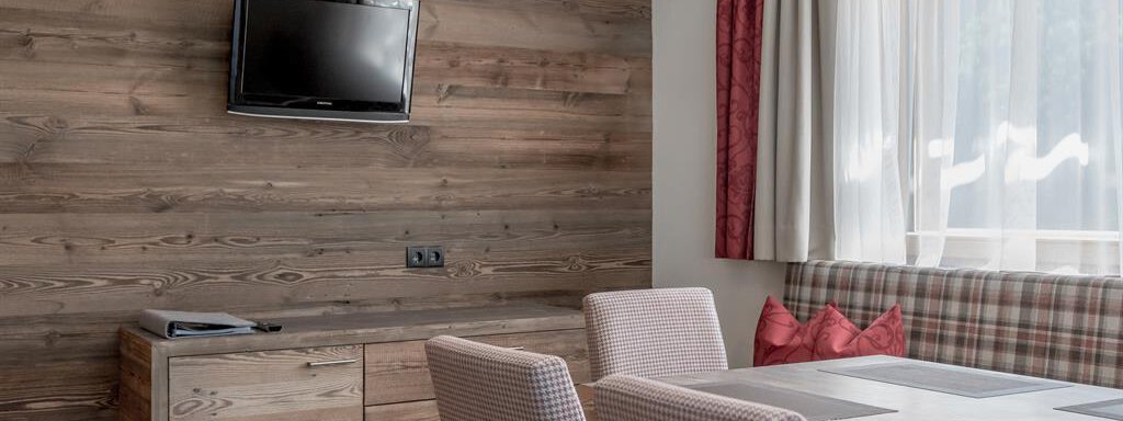 A modern room with wooden paneling and a flat-screen TV on the wall. The table is furnished with striped chairs and a cozy view through large windows. - The Peak Sölden - Sölden