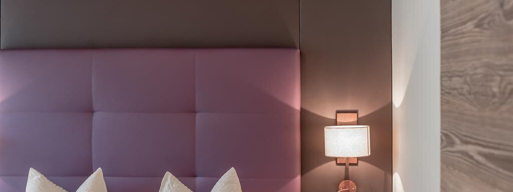 A modern bedroom with a purple headboard and elegant pillows. The soft lighting creates a relaxing atmosphere. - The Peak Sölden - Sölden