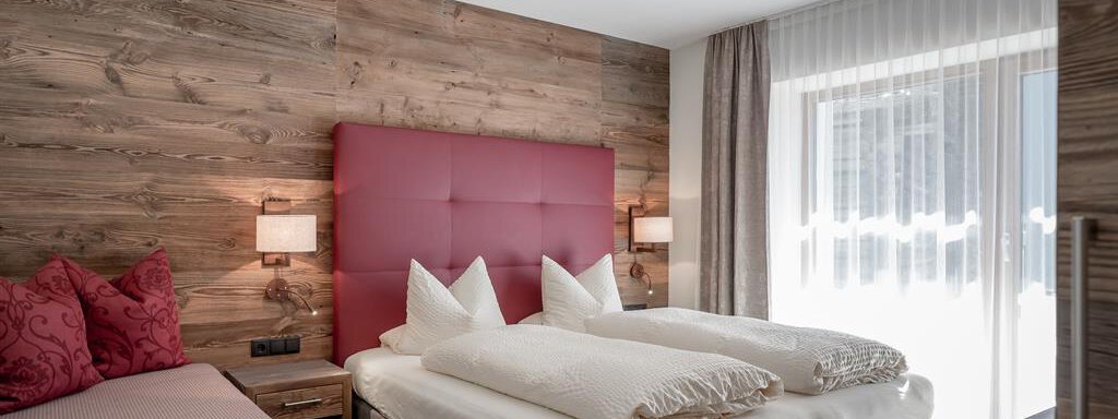 Schlafzimmer A modern bedroom with a cozy double bed and an additional single bed. The wall is made of wood, and large windows provide plenty of light. - The Peak Sölden - Sölden