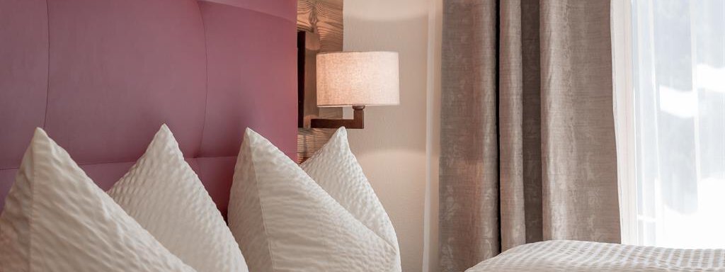 A cozy bedroom with two beds and large, decorative cushions. The walls are painted in neutral tones, and there is a soft glow from a lamp. - The Peak Sölden - Sölden