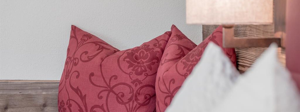 A cozy red pillow with elegant patterns and a bright lamp in the background. The warm atmosphere invites relaxation. - The Peak Sölden - Sölden