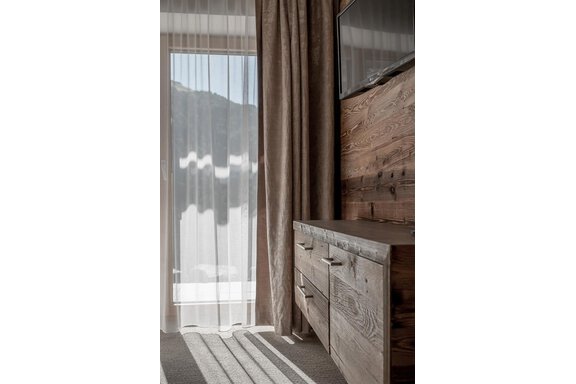 A cozy room with a wooden wardrobe and a window framed by a bright curtain. Gentle light falls on the floor and the walls. - The Peak Sölden - Sölden