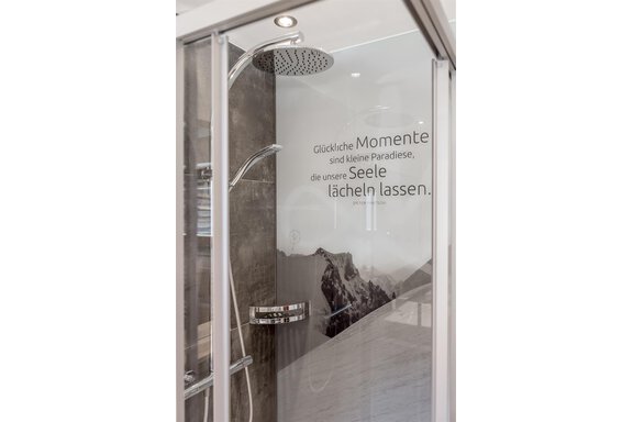 A modern shower cabin with a glass wall that displays an inspiring quote. In the background, an image of mountains is visible. - The Peak Sölden - Sölden