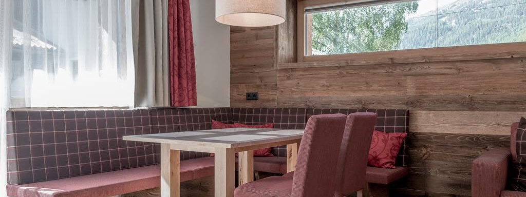 A cozy dining area with a wooden table and upholstered benches. Large windows offer a view of nature outside. - The Peak Sölden - Sölden