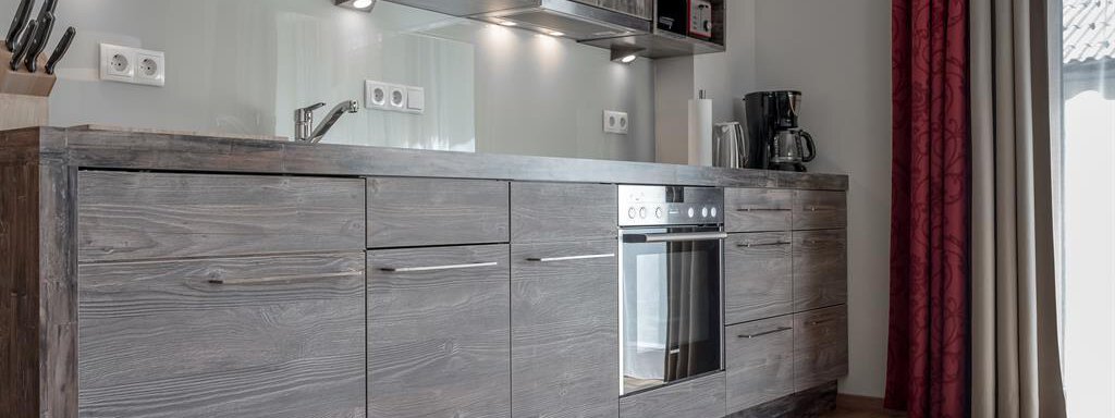 A modern kitchen with wooden cabinets and various appliances. The lighting creates a pleasant atmosphere. - The Peak Sölden - Sölden