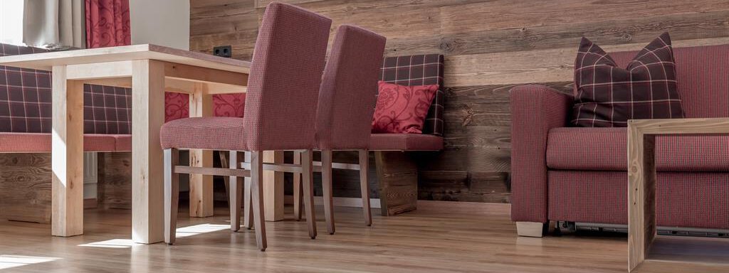 A cozy living area with a wooden table and several red chairs. The wooden paneling and the large window front create a warm ambiance. - The Peak Sölden - Sölden