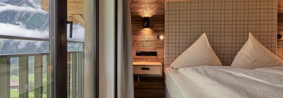 A stylish bedroom with wood decor and large windows. The view shows the mountains and the green landscape outside. - The Peak Sölden - Sölden