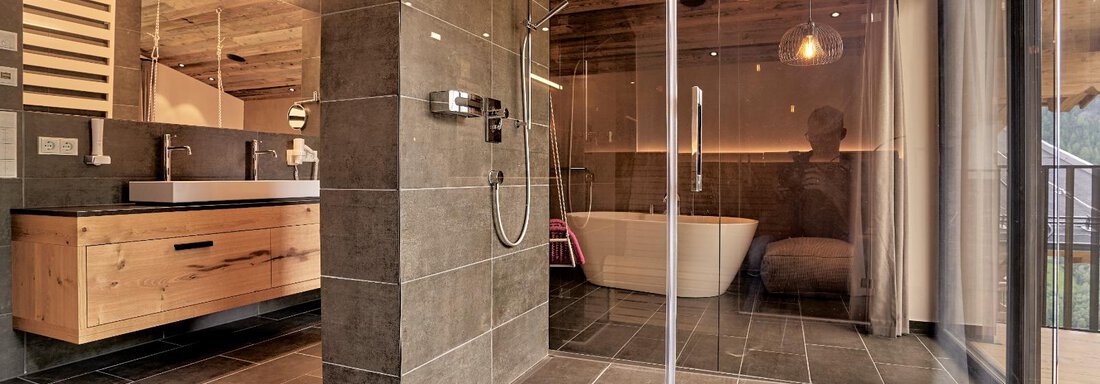 A modern bathroom with an open shower and a freestanding bathtub. The space combines dark tiles with wood-paneled walls for an elegant look. - The Peak Sölden - Sölden
