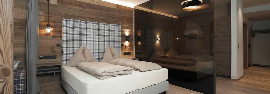 A modern bedroom with a double bed and wooden floor. The walls are partly made of wood, and there is elegant lighting. - The Peak Sölden - Sölden