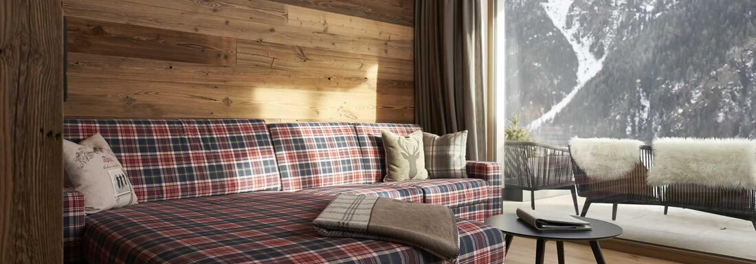 A cozy living room with a plaid sofa and a large window overlooking the mountains. The space has wooden paneling and a modern, inviting style. - The Peak Sölden - Sölden