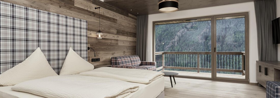 A modern hotel room with a cozy double bed and wood paneling. Large windows offer a beautiful view of the mountains. - The Peak Sölden - Sölden