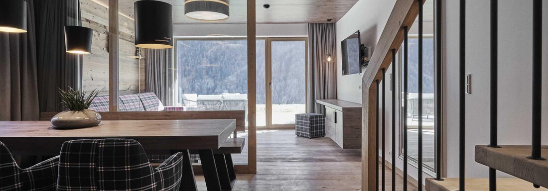 A modern living room with a large dining table and stylish chairs. Large windows offer a view of the landscape. - The Peak Sölden - Sölden