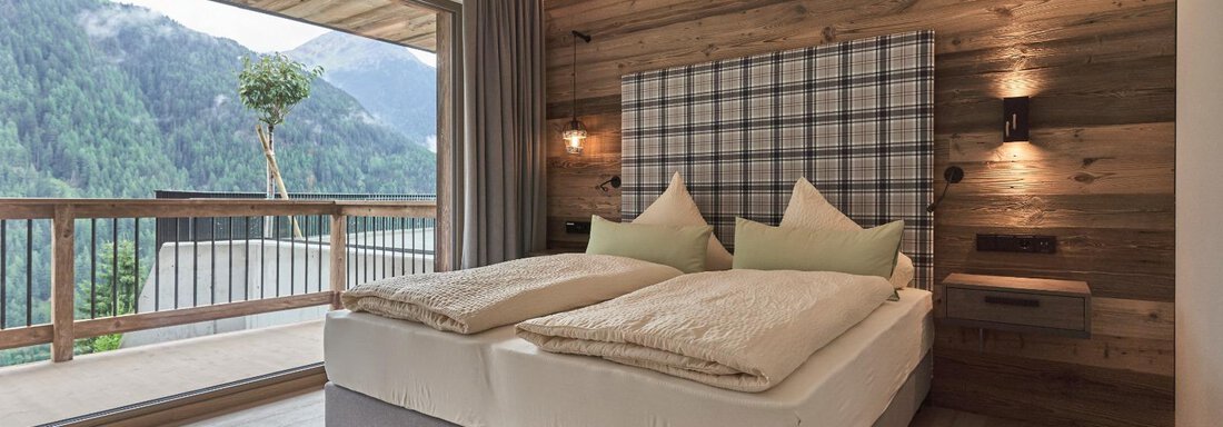 A modern bedroom with a double bed and wood-paneled walls. The balcony offers a view of the mountains and nature. - The Peak Sölden - Sölden