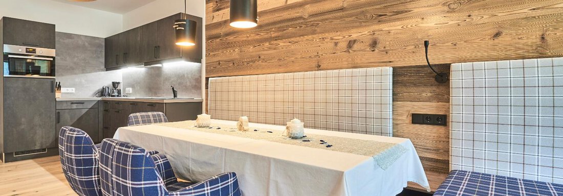 A modern dining area with a white table and checkered chairs. The walls are covered with wood, and the lighting creates a cozy atmosphere. - The Peak Sölden - Sölden