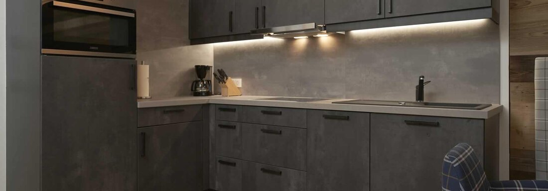 A modern kitchen with dark cabinets and sleek appliances. The lighting creates a pleasant atmosphere. - The Peak Sölden - Sölden