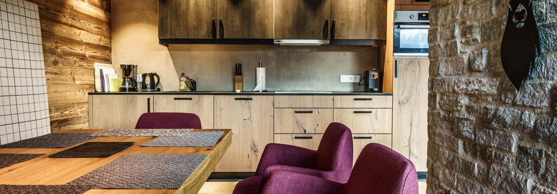 A modern kitchen with wooden shelves and a large dining table. Red chairs complement the warm, welcoming space. - The Peak Sölden - Sölden