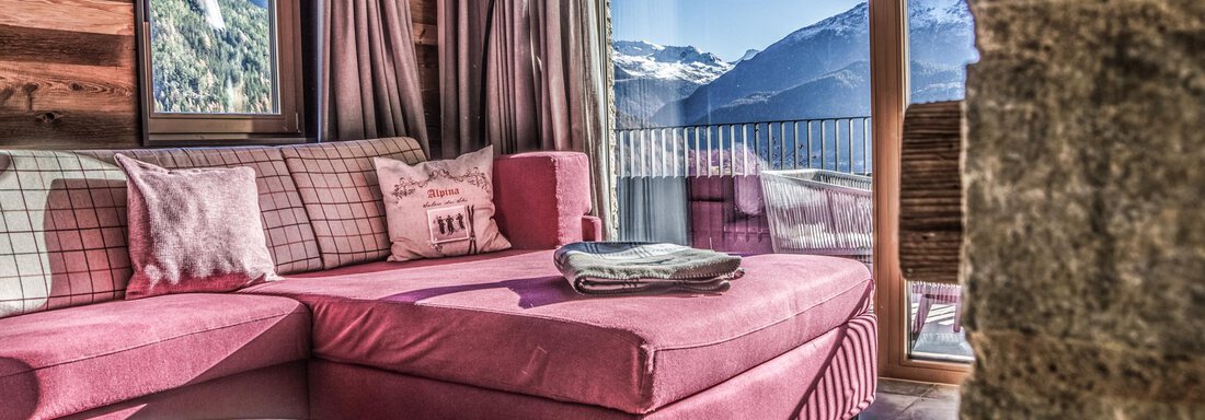 A modern living room with a pink sofa and large windows that offer a view of the mountains. The warm wooden paneling and cozy furnishings create an inviting atmosphere. - The Peak Sölden - Sölden