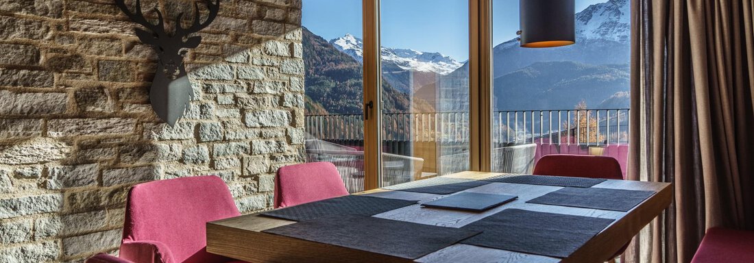 A modernly furnished dining area with a wood and stone interior. Large windows provide a view of the mountains. - The Peak Sölden - Sölden