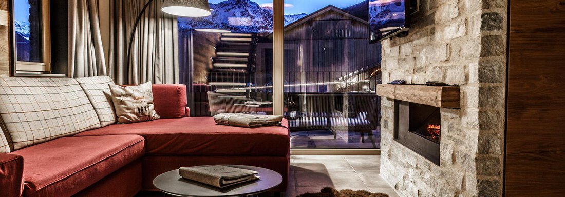 A modern living room with a red couch and a round table. Large windows offer a view of the mountains and provide plenty of daylight. - The Peak Sölden - Sölden