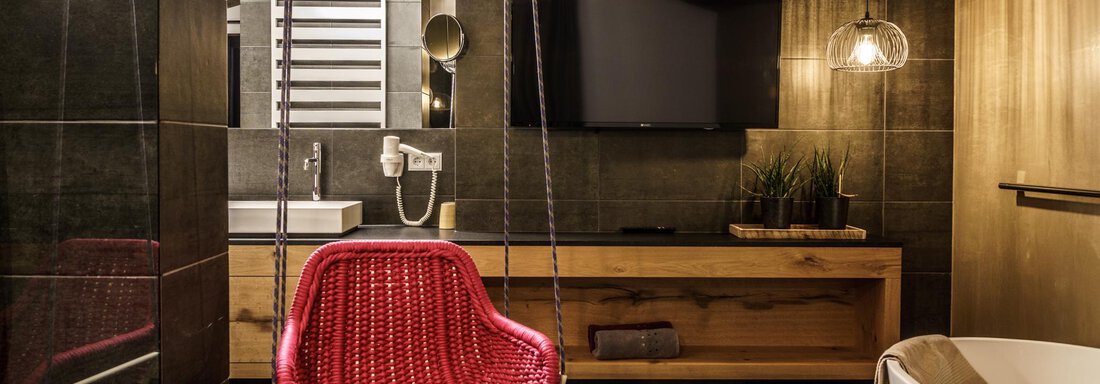 A modern bathroom with a red hanging swing chair and elegant furnishings. The design combines wood and dark tiles for a stylish atmosphere. - The Peak Sölden - Sölden