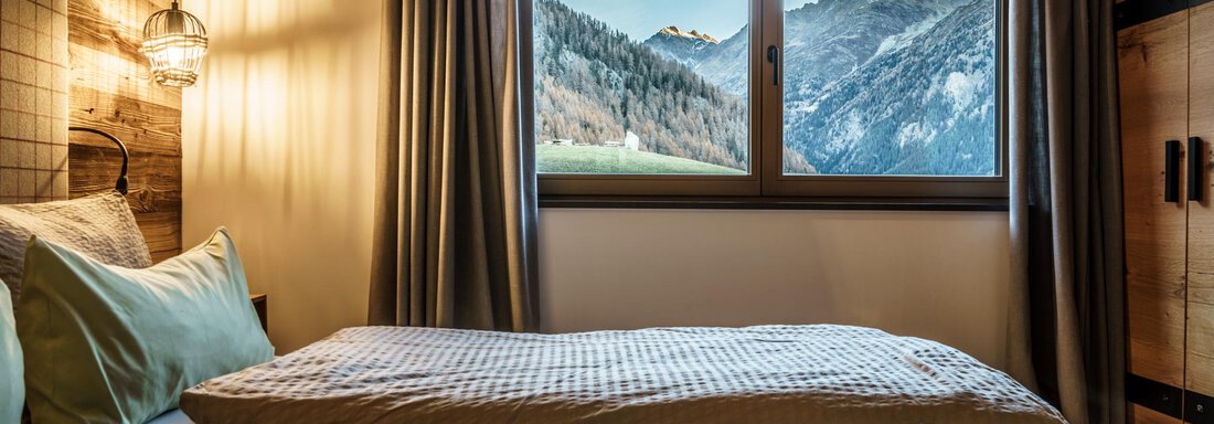 A cozy bedroom with two beds and a view of the mountains. The decor is modern and warm, with large windows and soft lighting. - The Peak Sölden - Sölden