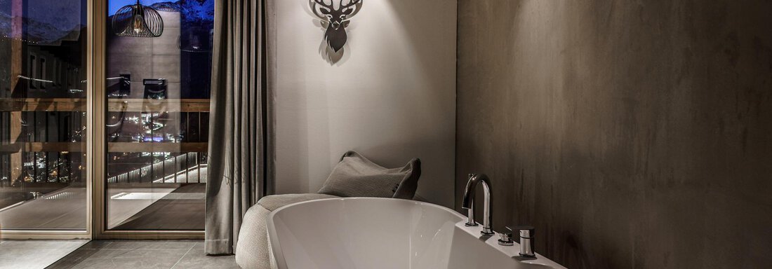 A modern bathroom with a freestanding bathtub and rustic wood decor. The view of the mountains and the large glass door create an inviting atmosphere. - The Peak Sölden - Sölden