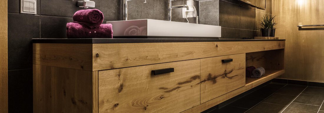 A modern bathroom with an elegant wooden vanity combination. The soft lighting and dark tiles create a relaxing atmosphere. - The Peak Sölden - Sölden
