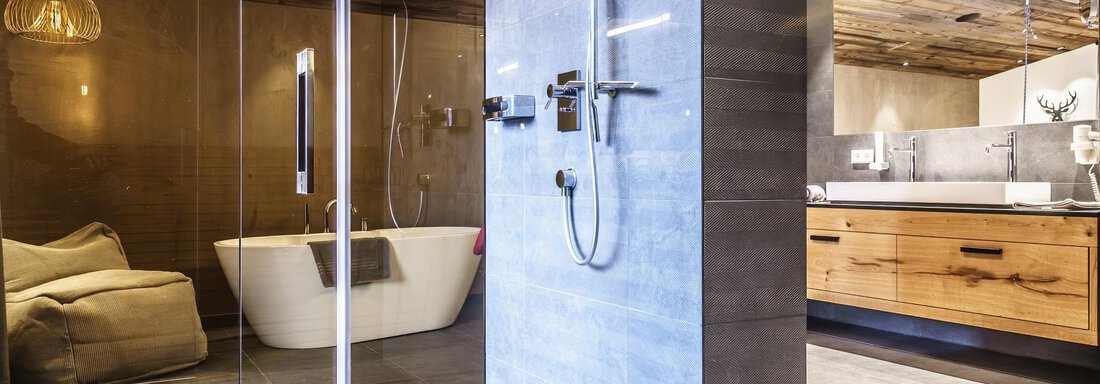 A modern bathroom with a freestanding bathtub and a large shower. The warm wooden elements and the soft lighting create a relaxed atmosphere. - The Peak Sölden - Sölden