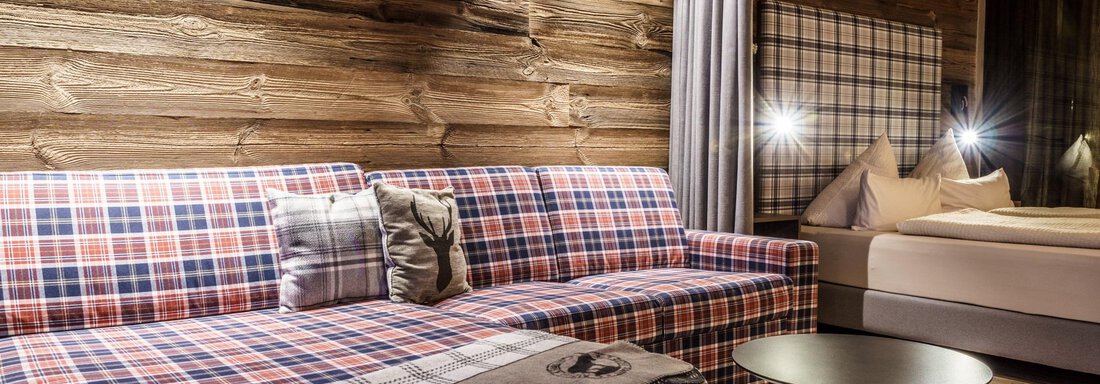 A cozy living room setup with a checked sofa and a round table. The wooden paneling on the wall gives the room a warm atmosphere. - The Peak Sölden - Sölden