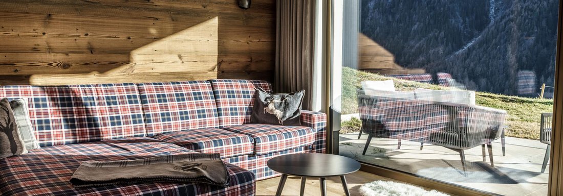 A cozy living room with a checked couch and a table. Large windows offer a view of the mountains and let in plenty of light. - The Peak Sölden - Sölden